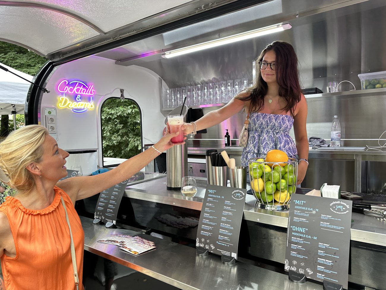 Ausgabe eines Cocktails über den Tresen des Trailers, daneben die Getränkekarte.