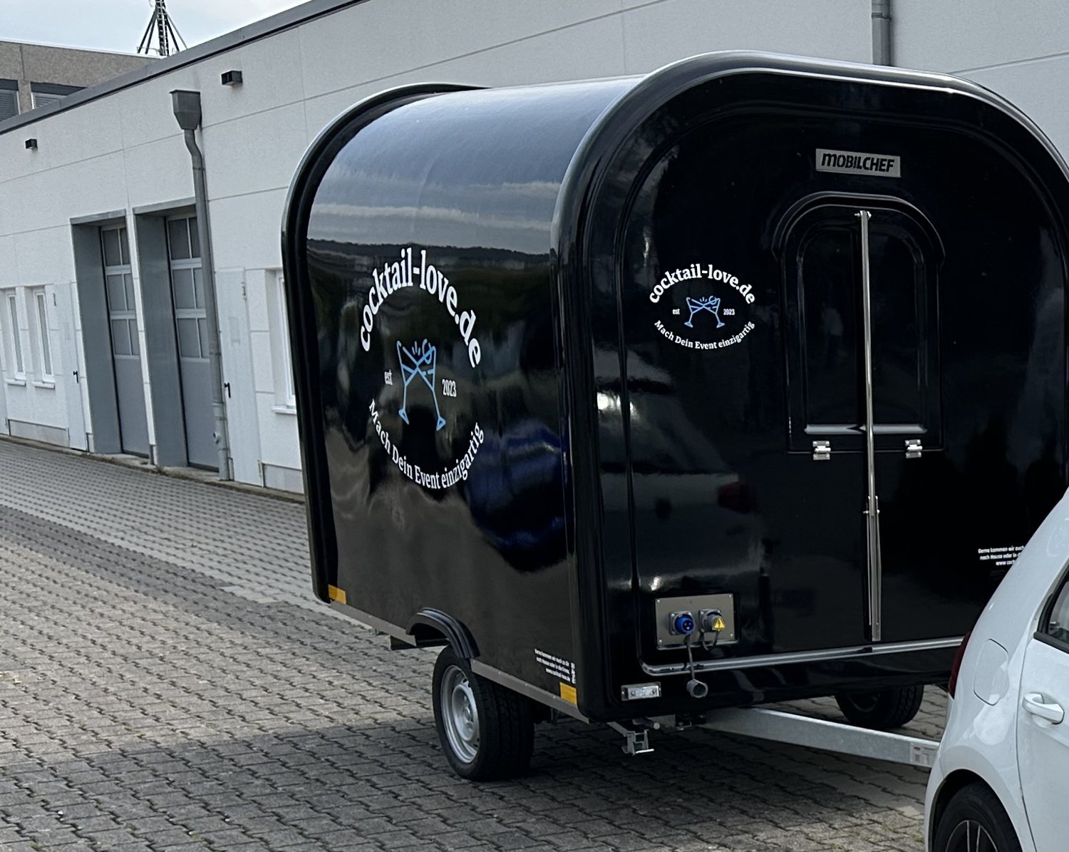 Der schwarze Cocktail-Trailer mit dem Logo auf der Seitenwand, angehängt an ein Zugfahrzeug.